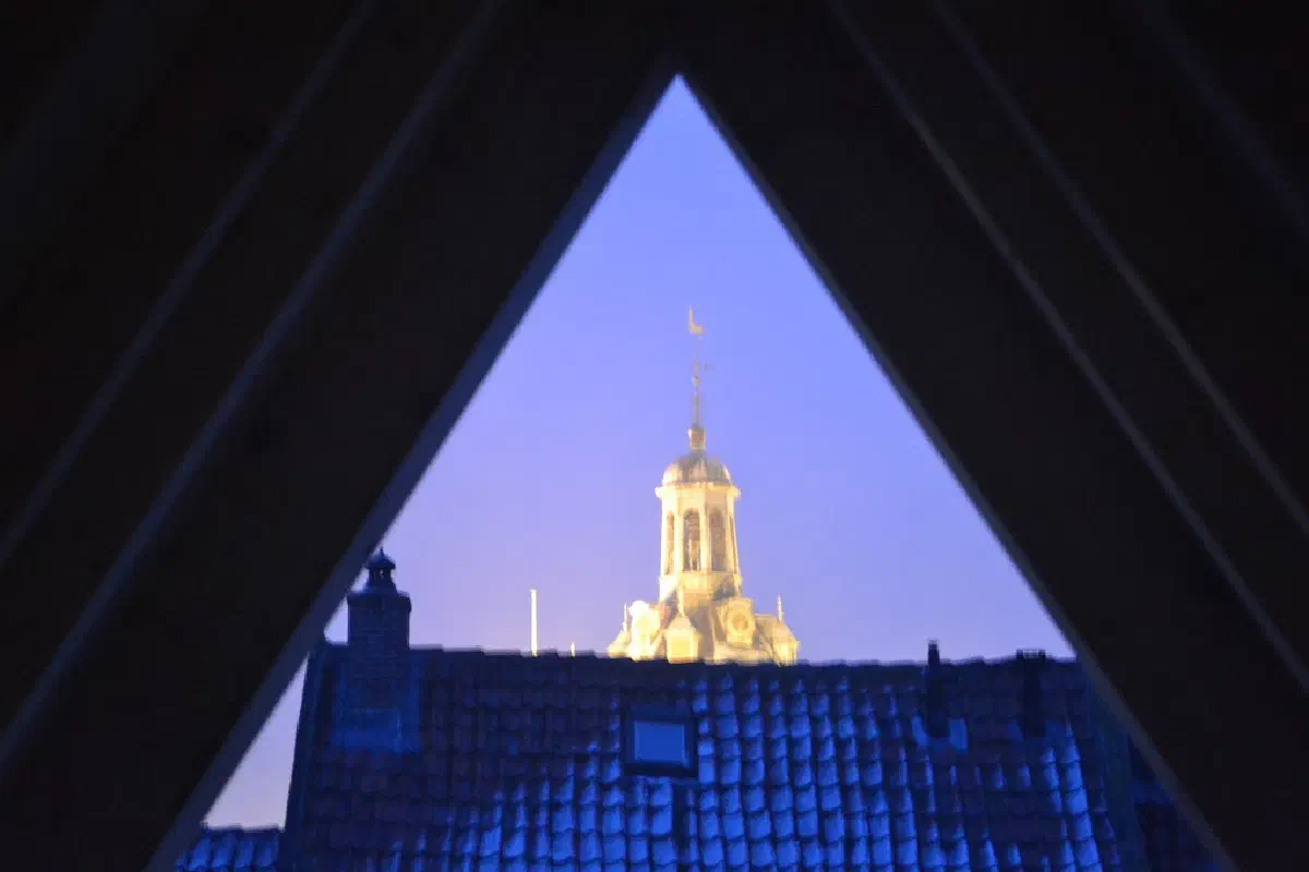 Avondzicht door het driehoekige dakraam op de verlichte Drommedaris